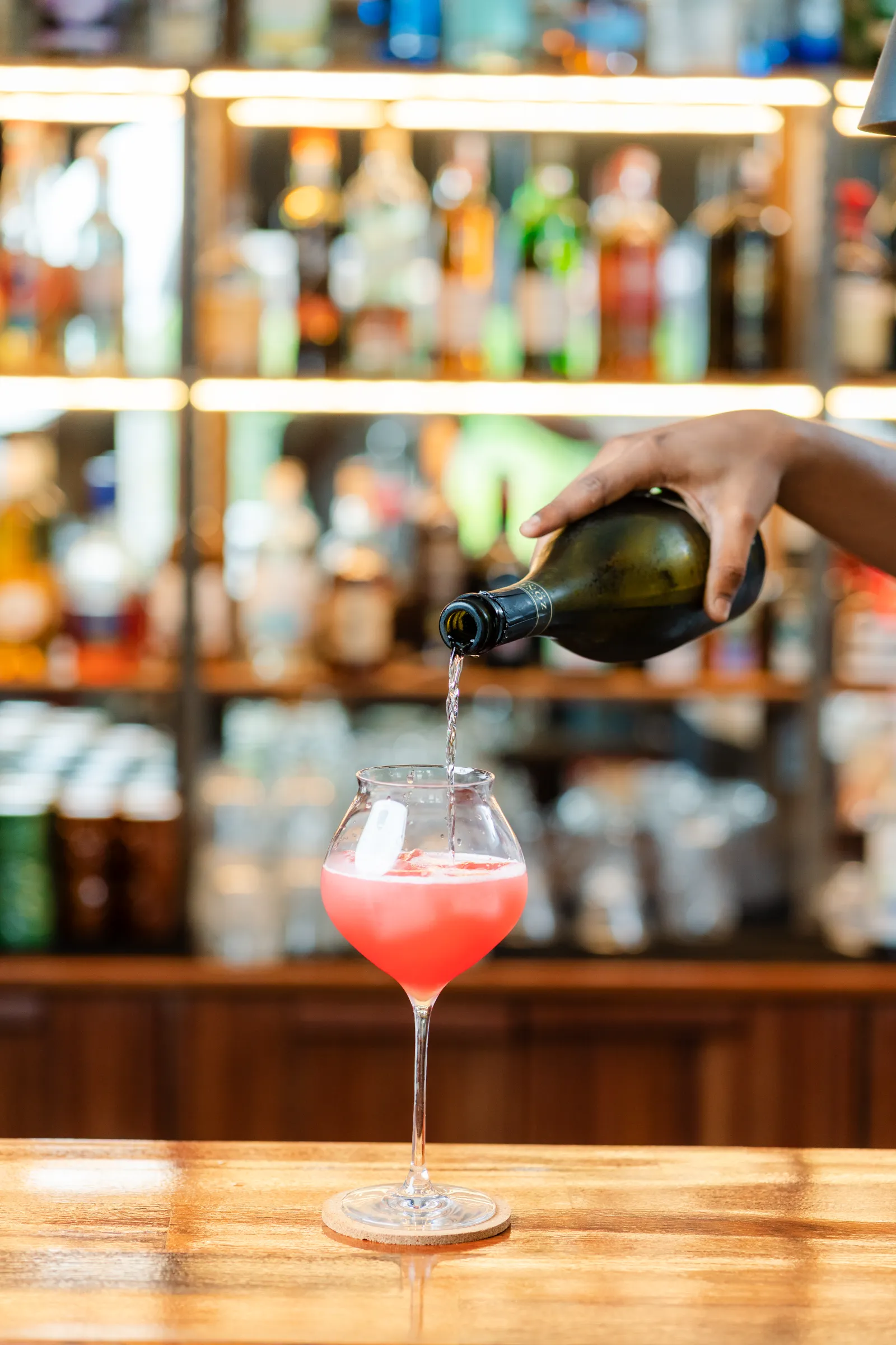 Prosecco poured into a pink cocktail at the bar