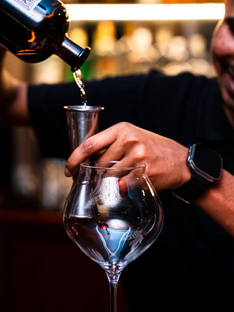 A bartender measuring a pour into a balloon glass