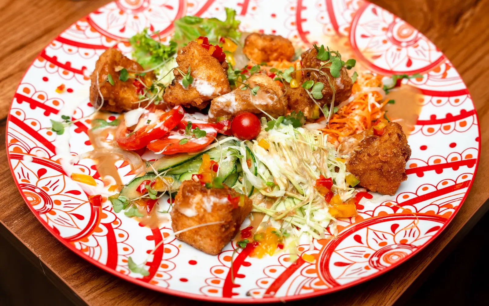 Crispy bites on salad, served on a red patterned plate