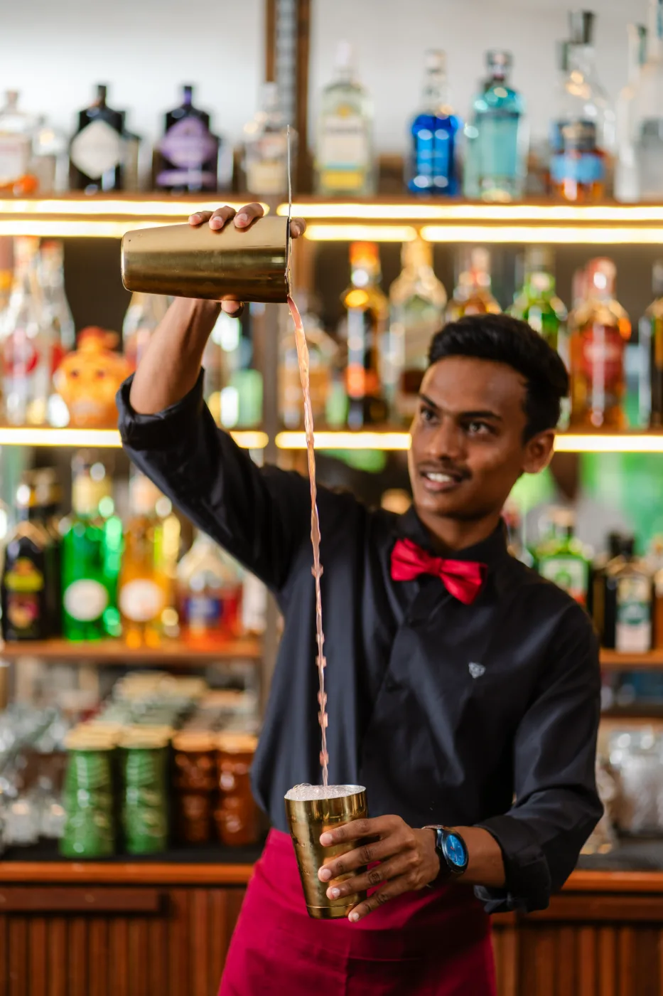 An Amigo Bar & Bistro bartender pouring a cocktail in a long stream from a brass tin