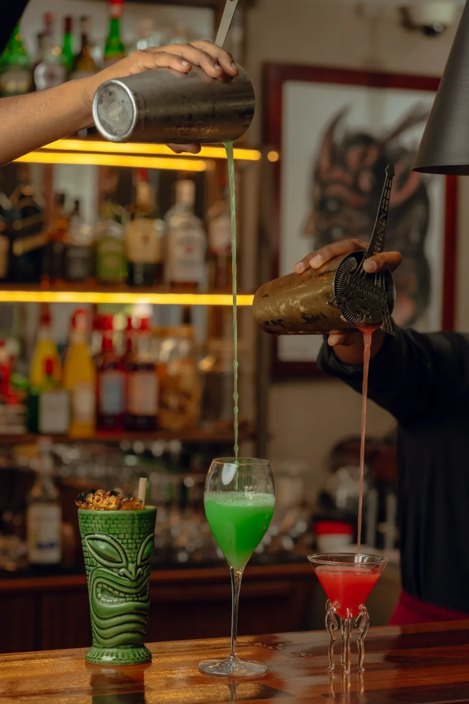 Two cocktails poured at once beside the carved green tiki mug