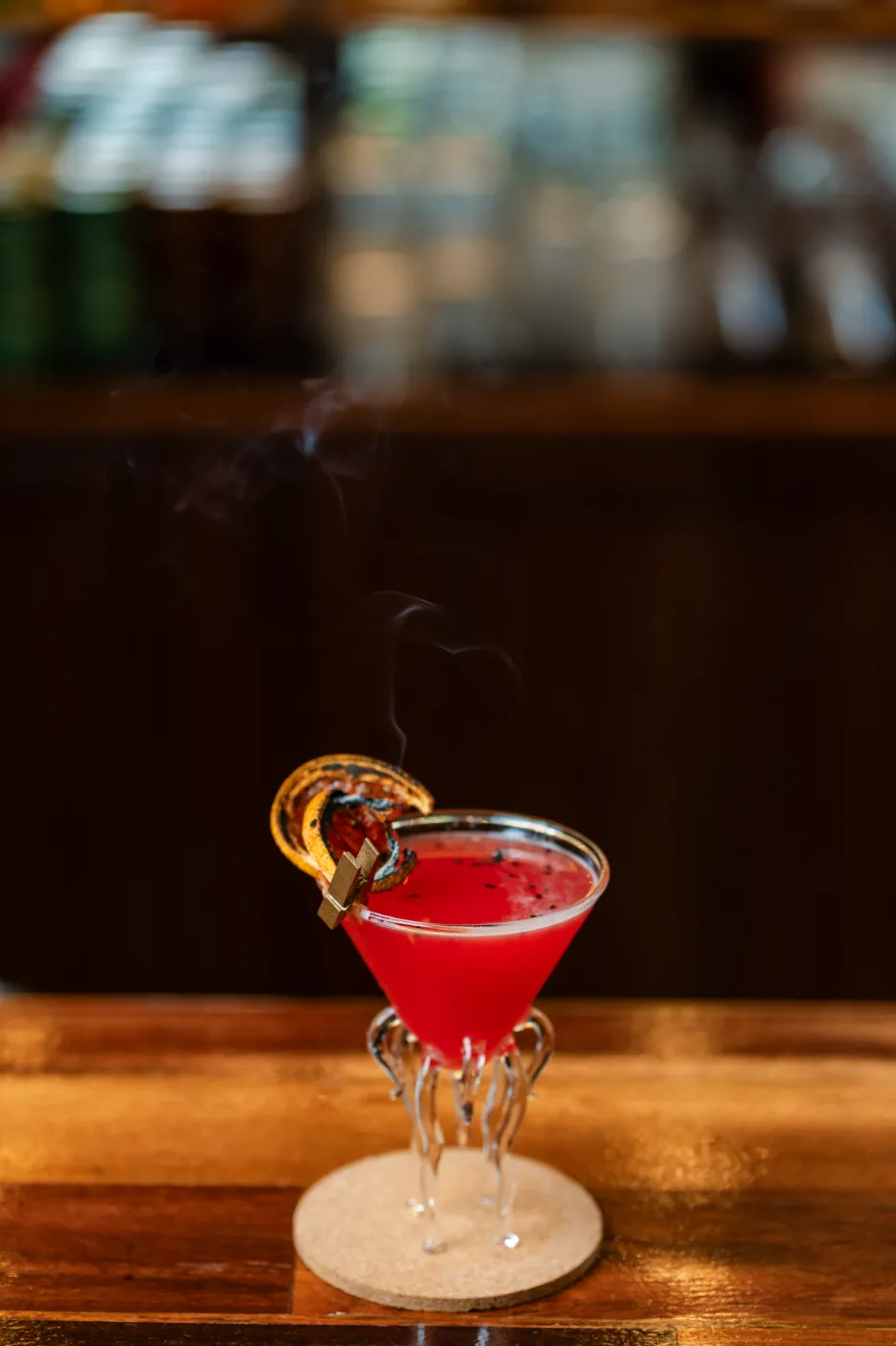 A red cocktail finished with a smoking charred orange wheel